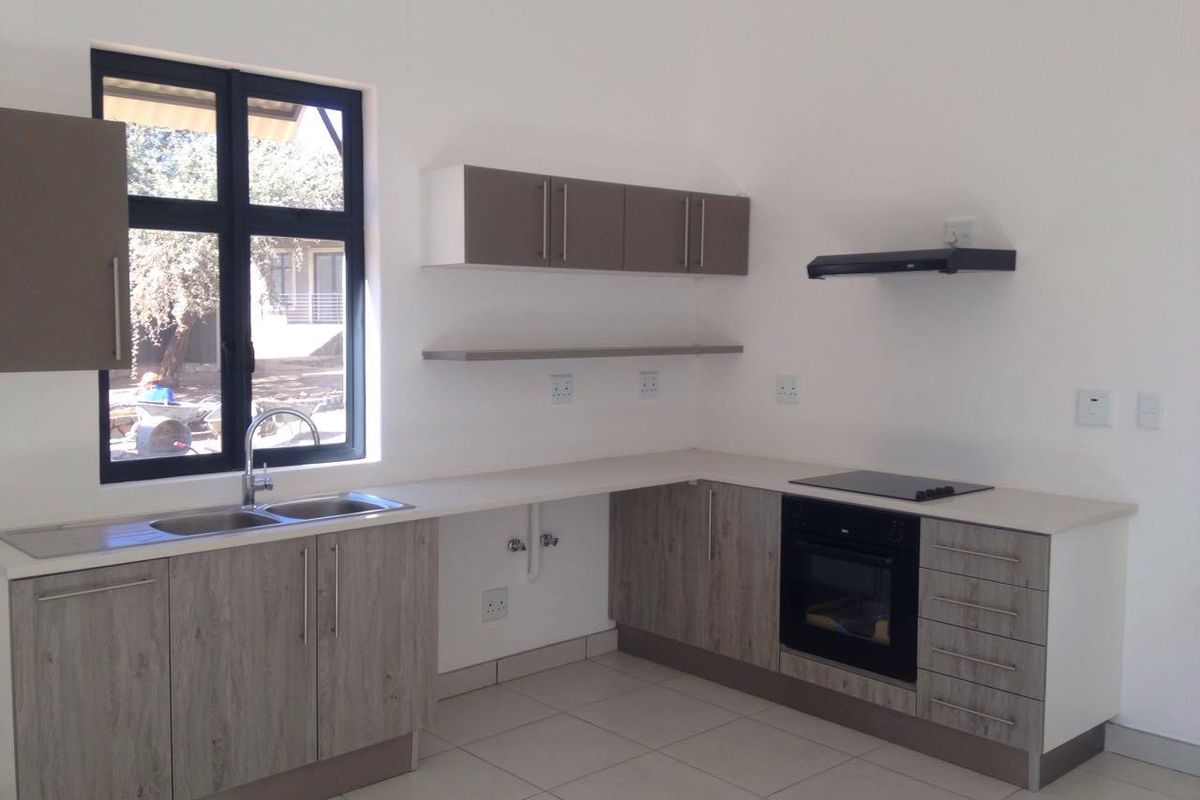 Modern kitchen featuring light wood-grain cabinetry, stone-look countertops, built-in oven, electric hob, extractor fan, and a double sink with a view.