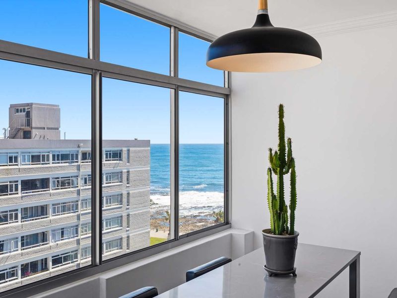 Bright living area featuring expansive floor-to-ceiling windows with direct ocean views and a modern pendant light fixture.