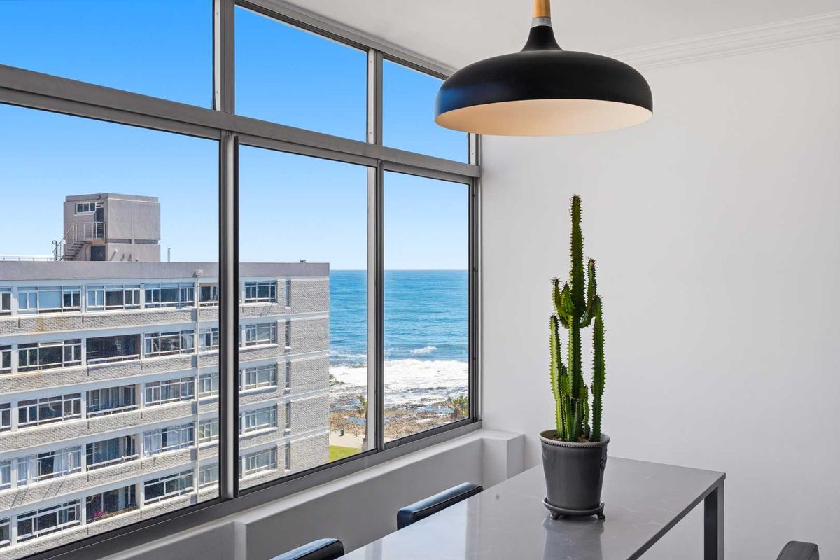 Bright living area featuring expansive floor-to-ceiling windows with direct ocean views and a modern pendant light fixture.