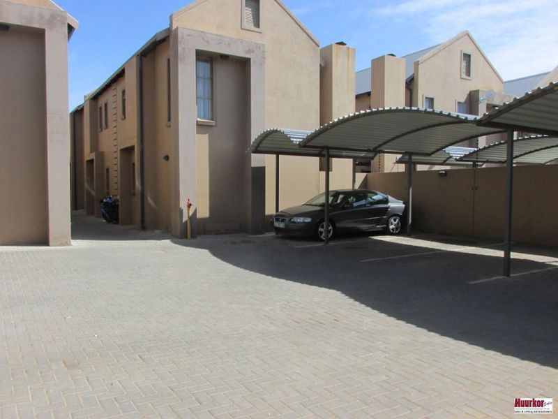 Exterior view of the apartment complex featuring a paved parking area with covered carports and multi-story residential units.