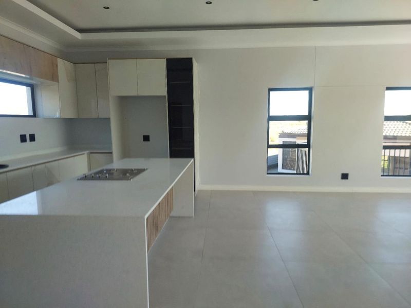 Modern open-plan kitchen and living area featuring a central island with stone countertops, sleek cabinetry, and large windows providing ample natural light.
