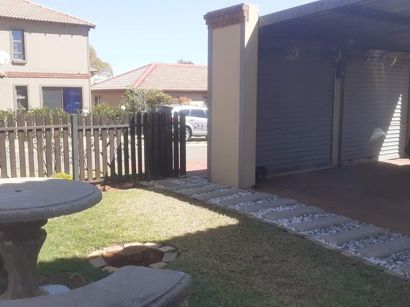 Front exterior view of the property featuring a double garage with roll-up doors, a paved driveway, and a small garden area with a stone pathway.