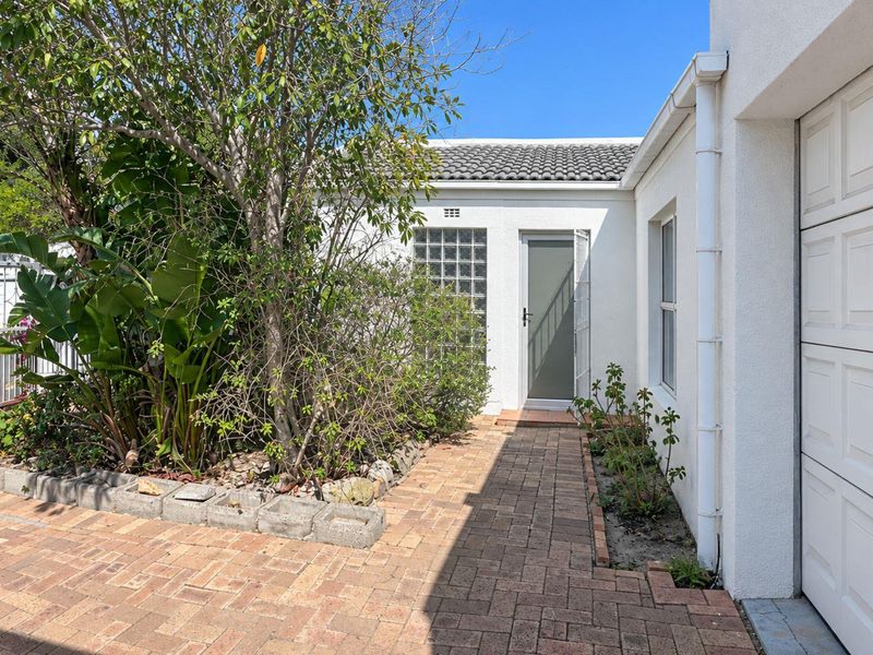 A well-maintained front entrance area featuring brick paving, a glass block window, and a clean white facade with a garage access point.