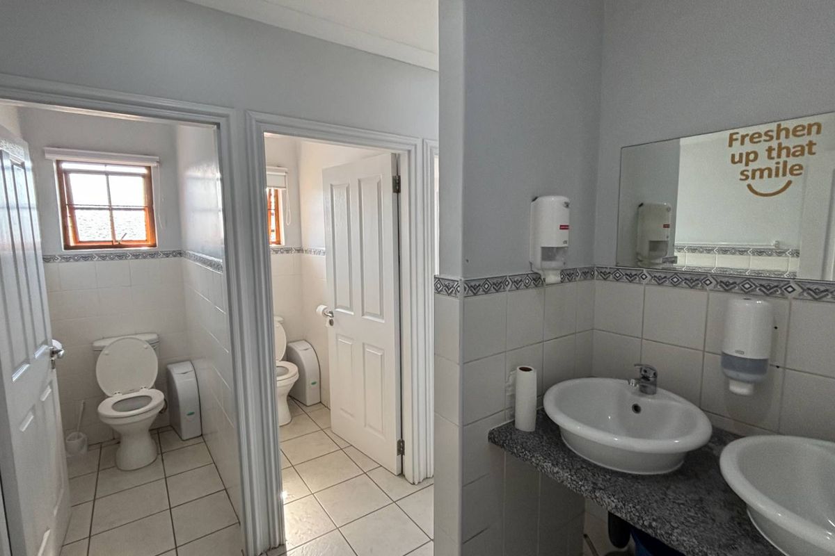 A functional office restroom facility featuring dual vanity basins, tiled walls with decorative borders, and two separate toilet cubicles.