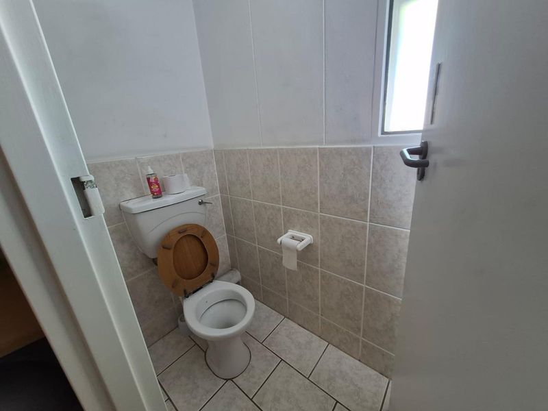 A compact, functional office restroom featuring neutral ceramic wall and floor tiling, a standard toilet, and a small window for natural light.