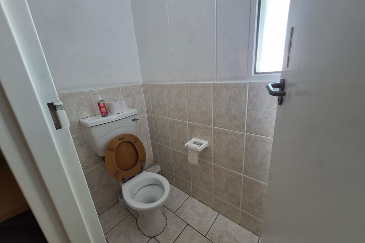 A compact, functional office restroom featuring neutral ceramic wall and floor tiling, a standard toilet, and a small window for natural light.