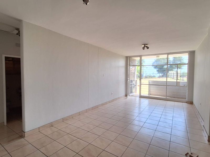 A bright, empty living room featuring neutral tiled flooring and a large glass sliding door providing natural light and access to the exterior.