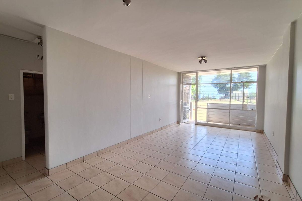 A bright, empty living room featuring neutral tiled flooring and a large glass sliding door providing natural light and access to the exterior.