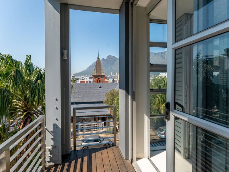 A modern balcony featuring timber decking and a metal balustrade, offering clear views of the surrounding cityscape and mountain backdrop.