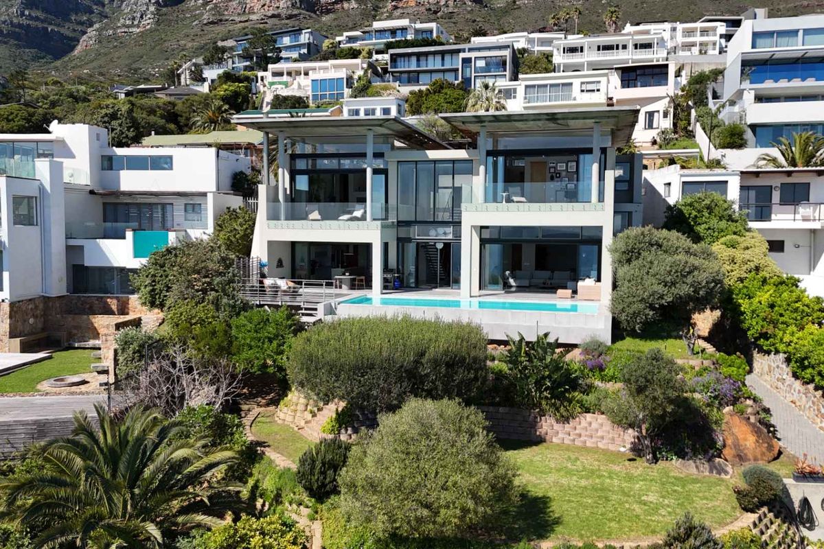 Aerial view of a modern multi-level luxury residence featuring a swimming pool, expansive glass facades, and tiered landscaped gardens set against a mountain backdrop.