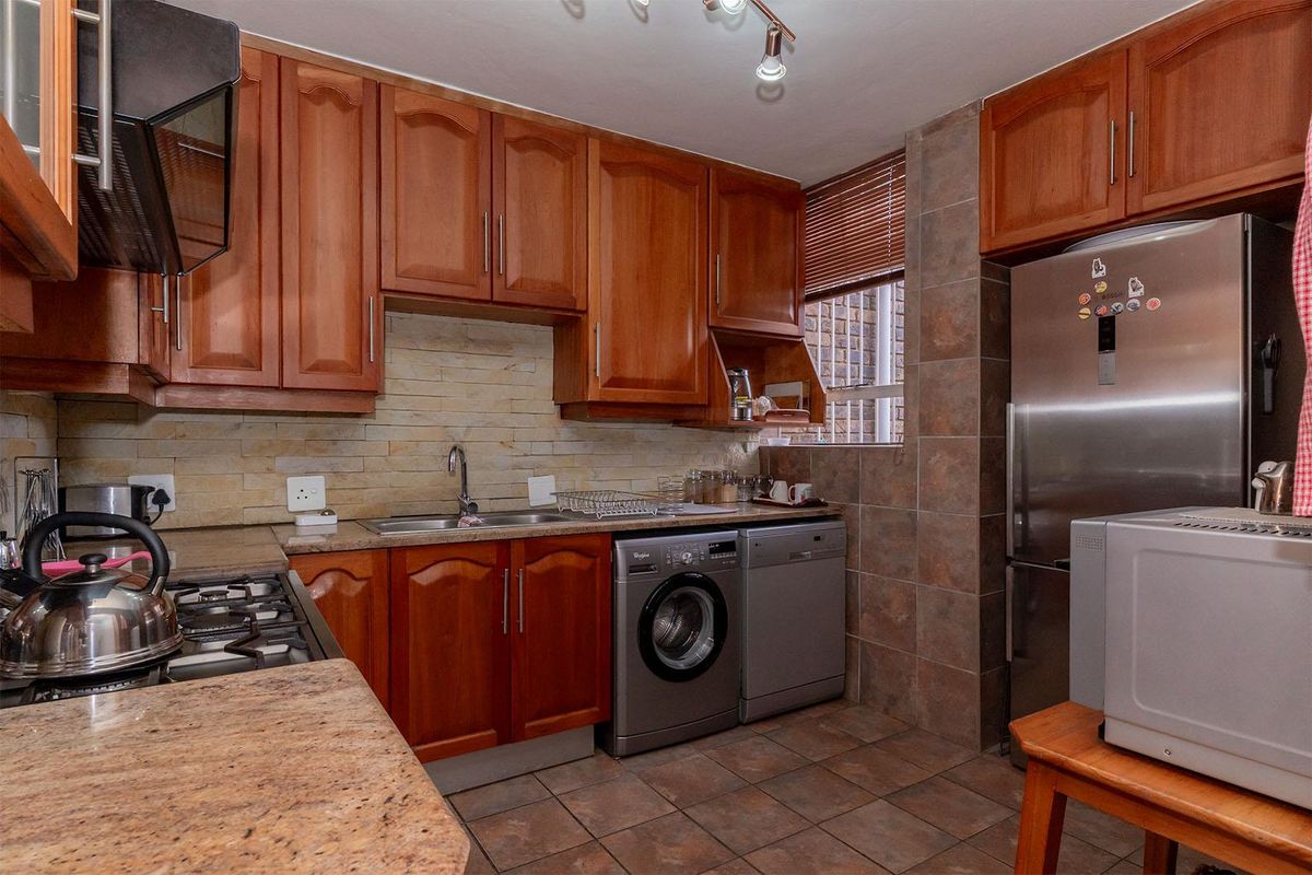 A functional kitchen featuring wooden cabinetry, granite countertops, a stone-tiled backsplash, and integrated space for laundry appliances.