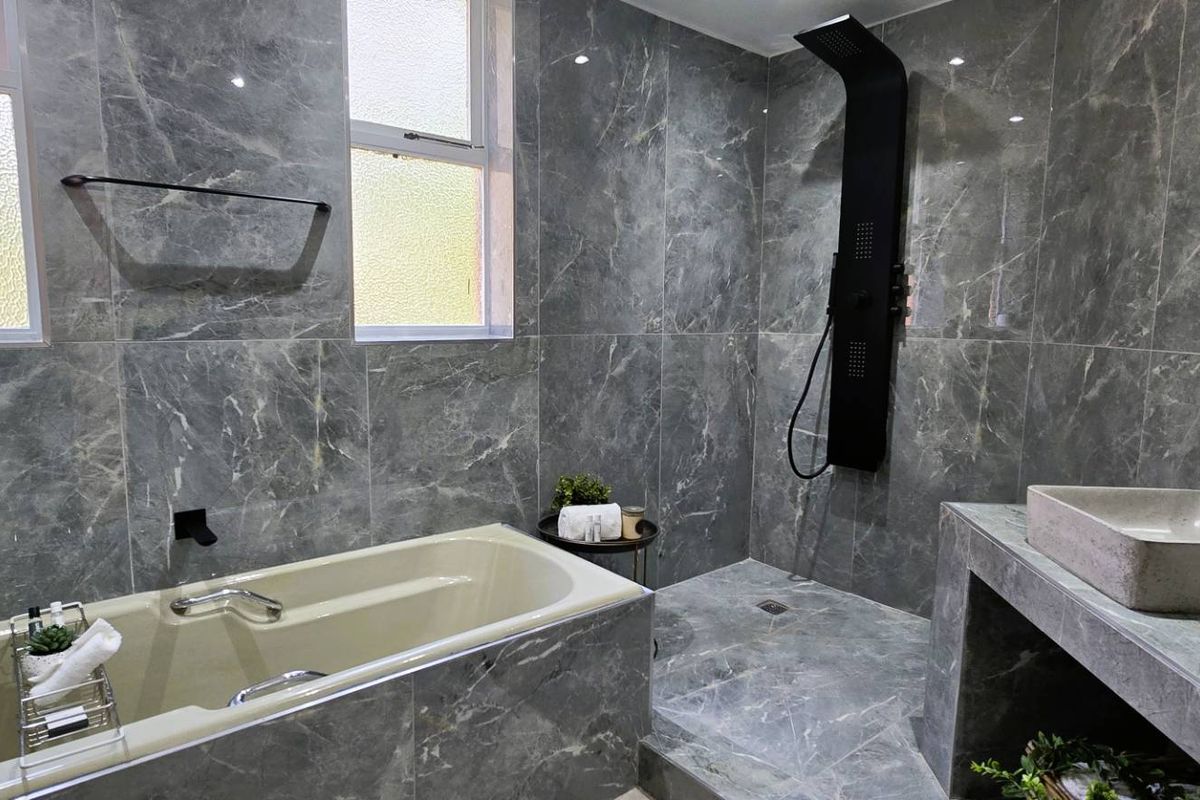 Modern bathroom featuring marble-look wall tiles, a built-in bathtub, a walk-in shower with a black panel, and a dual concrete vanity setup.
