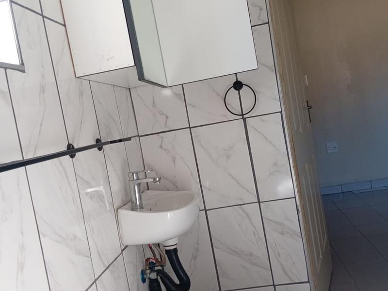 A small bathroom featuring tiled walls, a wall-mounted basin with exposed plumbing, and a medicine cabinet, requiring some maintenance and cosmetic updates.
