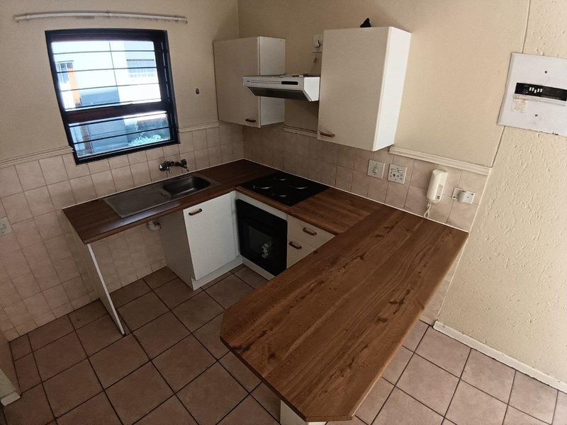 Compact kitchen featuring built-in cabinetry, laminate countertops, an electric hob, oven, and extractor fan with tiled flooring and splashbacks.