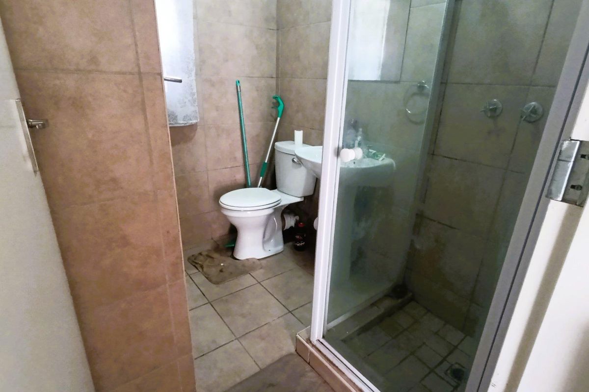 A compact bathroom featuring a pedestal basin, a standard toilet, and a glass-enclosed shower with full-height wall tiling.