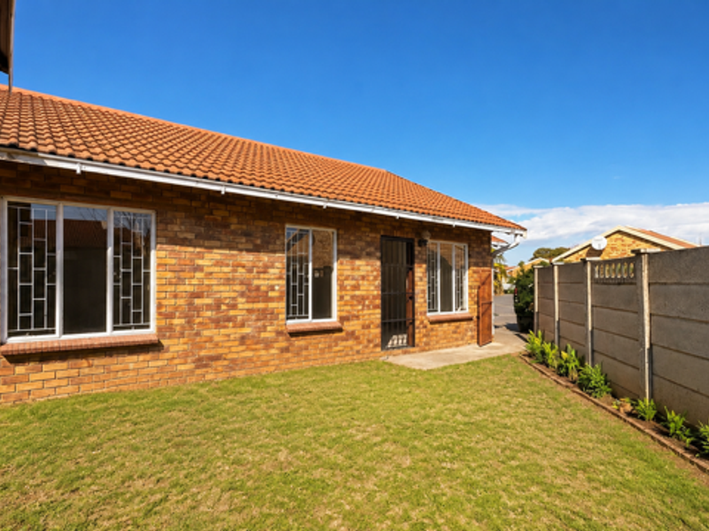 Rear view of the townhouse featuring a face brick exterior, tiled roof, security bars on windows, and a private lawn area with boundary wall.