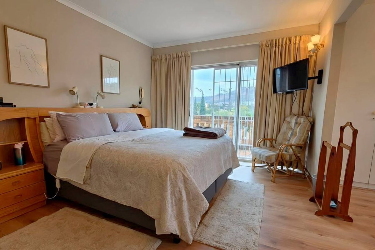 A well-lit bedroom featuring built-in cabinetry, laminate flooring, and sliding glass doors that open onto a private balcony with scenic views.