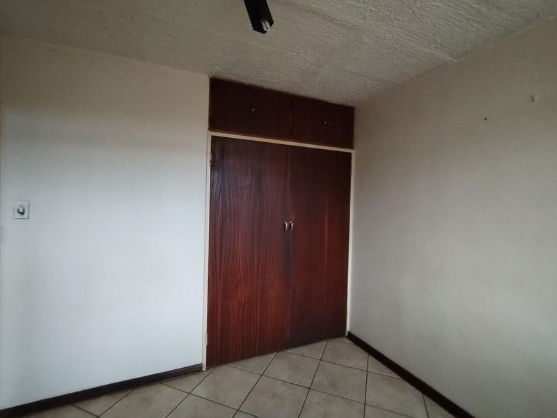 An empty bedroom featuring tiled flooring, a textured ceiling, and a dark wood built-in wardrobe with overhead storage compartments.