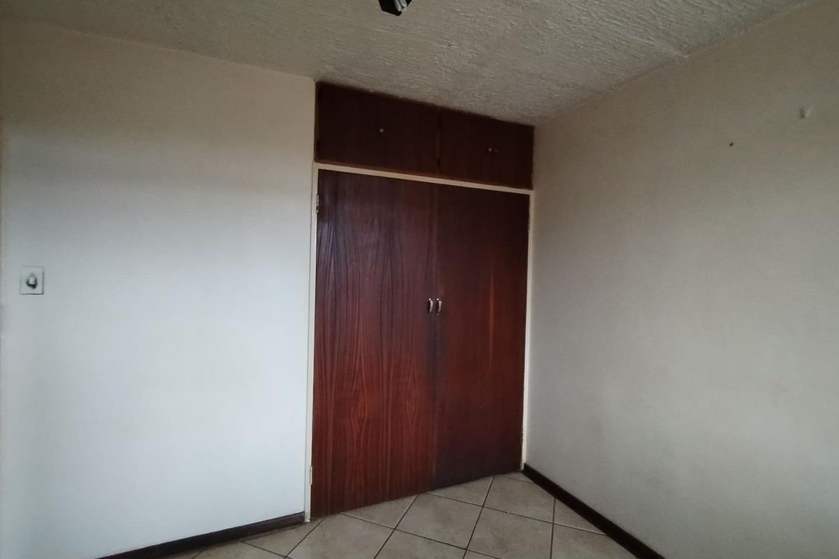 An empty bedroom featuring tiled flooring, a textured ceiling, and a dark wood built-in wardrobe with overhead storage compartments.