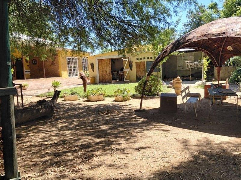 A spacious rear garden area featuring a covered patio, detached garage, and established trees, offering potential for outdoor living and landscaping improvements.