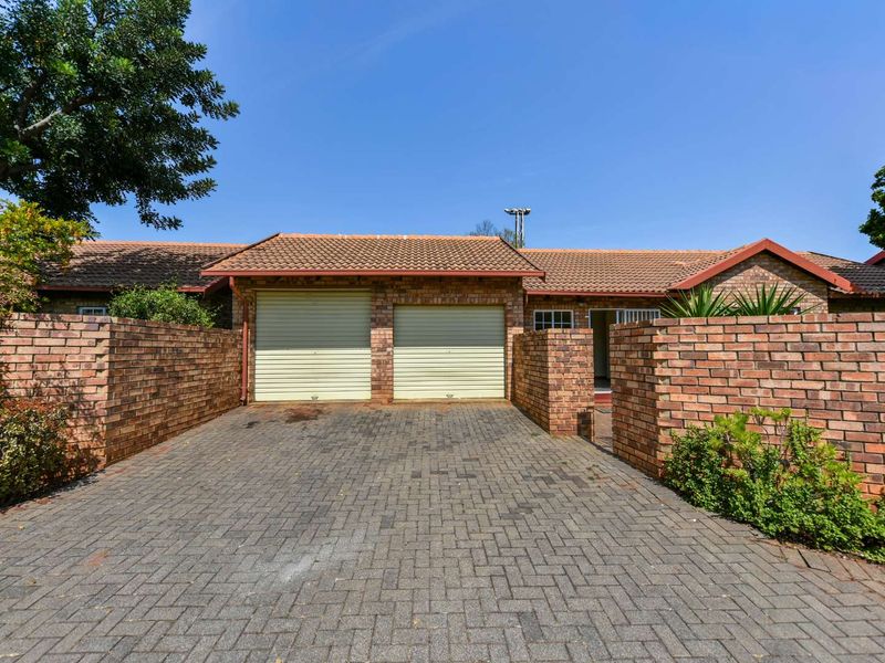 Front exterior view of a townhouse featuring a double garage, paved driveway, and brick boundary walls under a tiled roof.