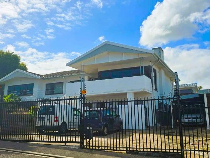Front exterior view of a two-story house featuring a balcony, attached garage, and secure metal gate entrance.