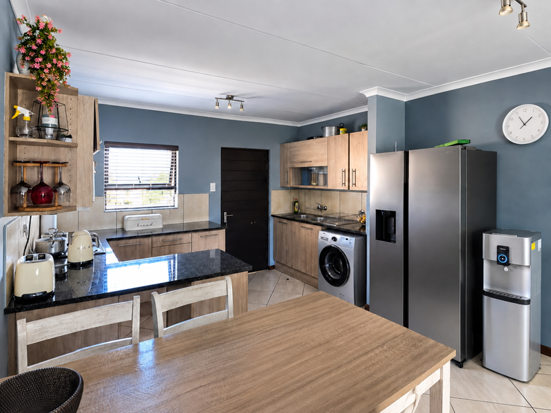 A functional kitchen featuring wood-look laminate cabinetry, dark granite countertops, tiled backsplash, and integrated laundry plumbing, offering a clean and practical workspace.