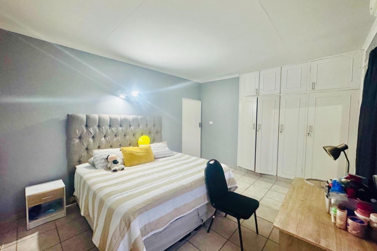 A spacious bedroom featuring built-in cupboards, tiled flooring, and neutral wall finishes, offering a functional and comfortable living space.