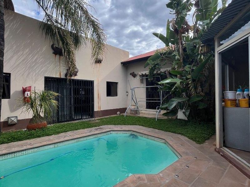 Outdoor pool area featuring a tiled patio, established garden, and direct access to the home via sliding doors with security gates.