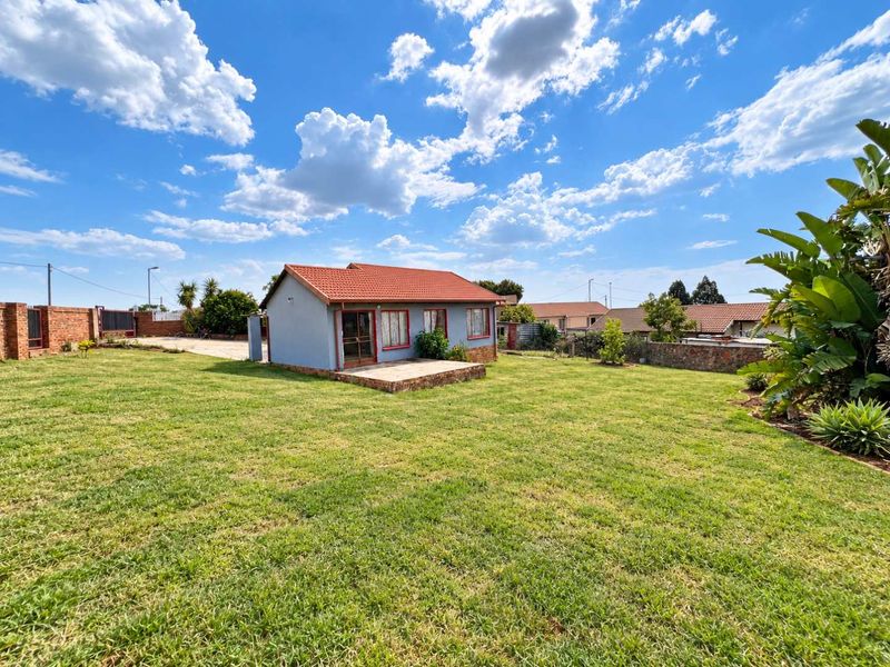 A view of the rear exterior of the house featuring a tiled roof, a paved patio area, and a spacious surrounding lawn.