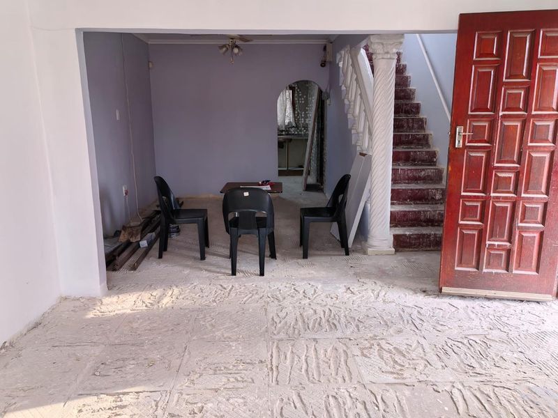 An entry area featuring a staircase with a decorative column, leading to an archway. The space is currently undergoing renovation with unfinished flooring.