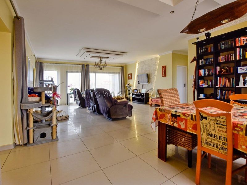 Spacious open-plan living and dining area featuring large format floor tiles, decorative ceiling details, and a stone feature wall with sliding door access.