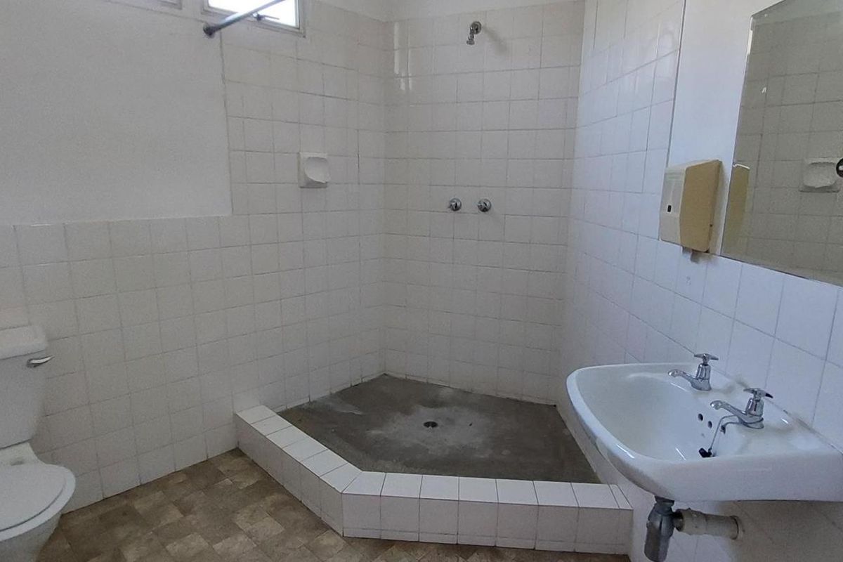 A dated bathroom featuring a tiled shower enclosure, pedestal basin, and toilet, requiring renovation to update the finishes and fixtures.