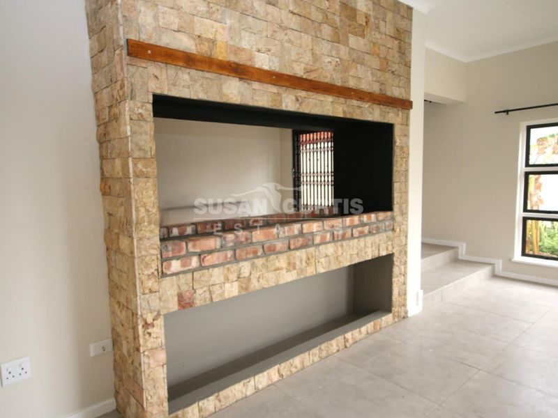 Spacious living area featuring a prominent stone-clad built-in fireplace and neutral tiled flooring, offering a clean and modern aesthetic.