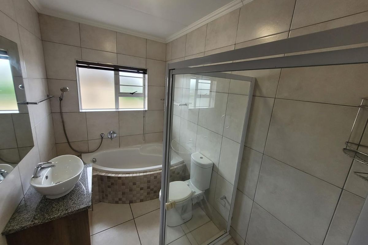 A functional bathroom featuring a corner bathtub, a separate glass-enclosed shower, a vessel sink vanity, and neutral wall and floor tiling.