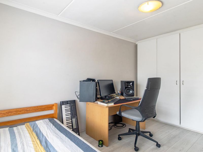 A functional bedroom featuring light-toned laminate flooring, a built-in wardrobe, and neutral wall finishes, suitable for use as a bedroom or home office.