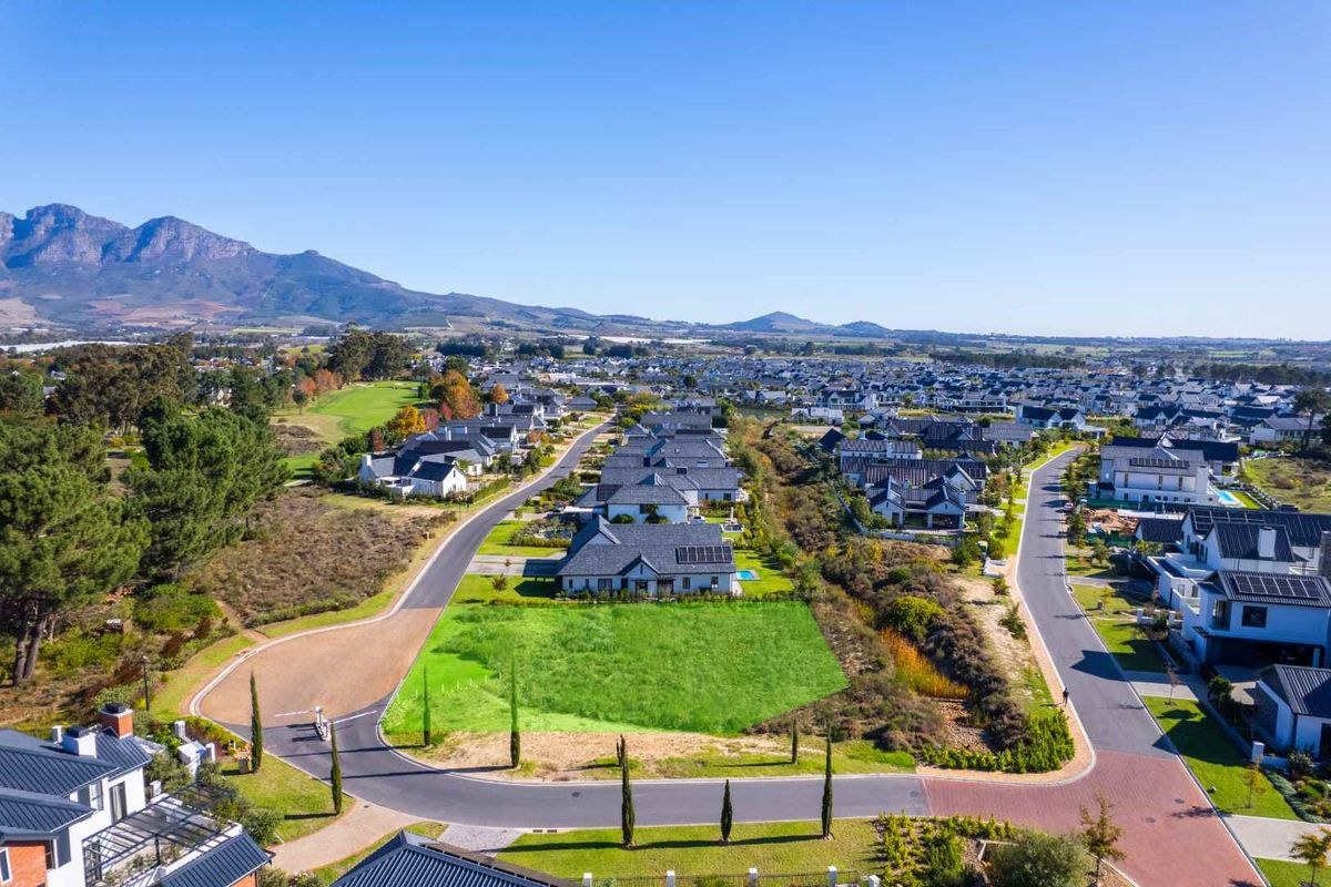An elevated aerial view of a residential estate featuring vacant land plots, paved roads, and surrounding mountain landscape views.