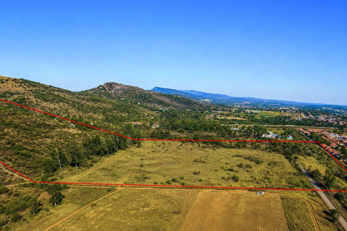 An aerial view of a large, undeveloped farm plot featuring natural landscape, rolling hills, and clearly marked property boundaries.