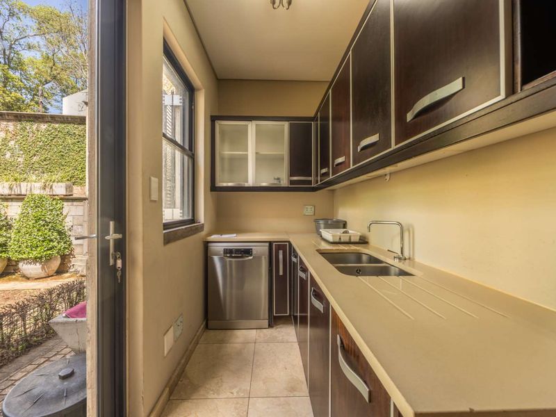 A functional scullery featuring dark wood cabinetry, stone countertops, a double basin sink, and an integrated dishwasher with direct access to the garden.