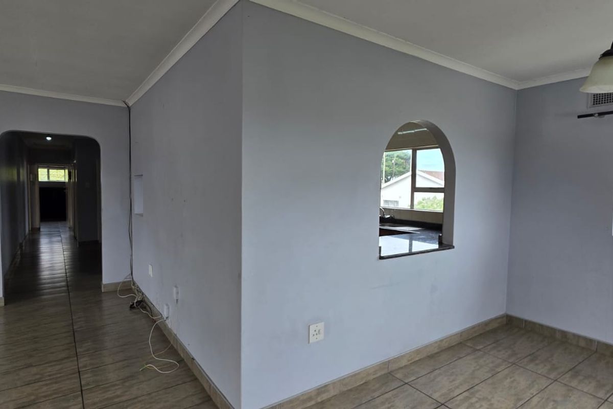An empty living area featuring tiled flooring, an arched pass-through window to the kitchen, and a hallway leading to the rest of the home.