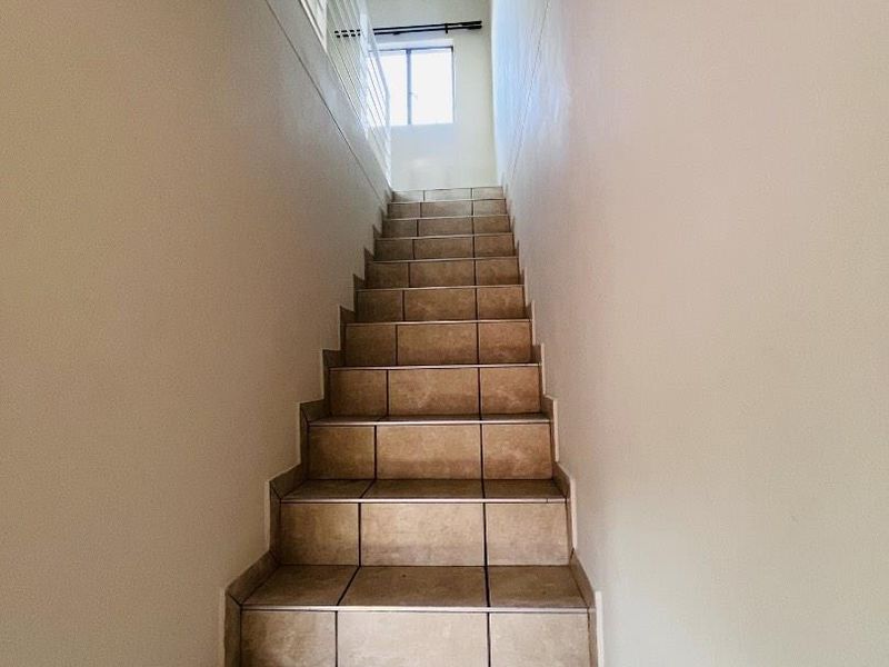 A staircase featuring tiled steps and a metal balustrade leading to an upper landing with natural light.