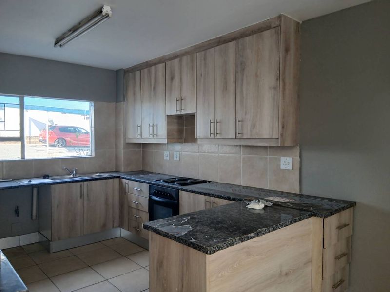 A functional kitchen featuring light wood-look cabinetry, dark laminate countertops, a built-in oven and hob, and tiled flooring.