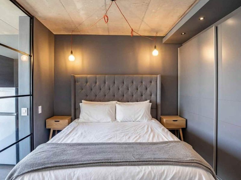 Modern bedroom featuring an exposed concrete ceiling, built-in sliding wardrobe, and a sleek glass partition wall, creating a contemporary and stylish living space.