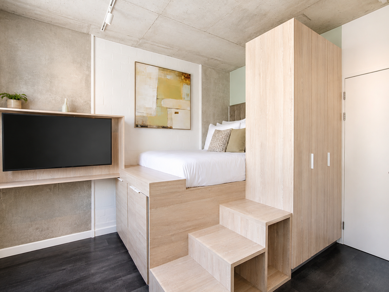 Modern bedroom featuring a custom built-in platform bed with integrated storage, light wood cabinetry, and an exposed concrete ceiling.