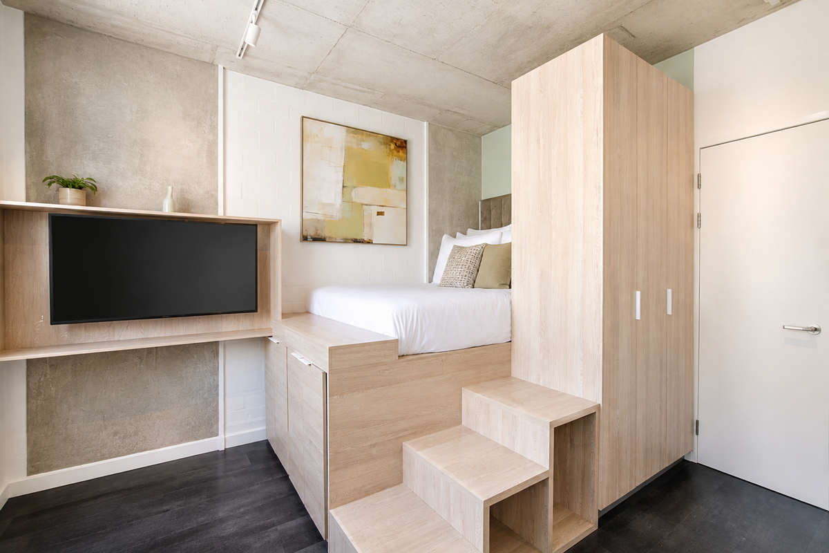 Modern bedroom featuring a custom built-in platform bed with integrated storage, light wood cabinetry, and an exposed concrete ceiling.