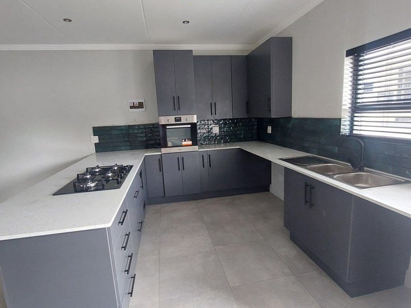 Modern kitchen featuring dark grey cabinetry, white quartz countertops, a gas hob, built-in oven, and a double sink with a tiled backsplash.