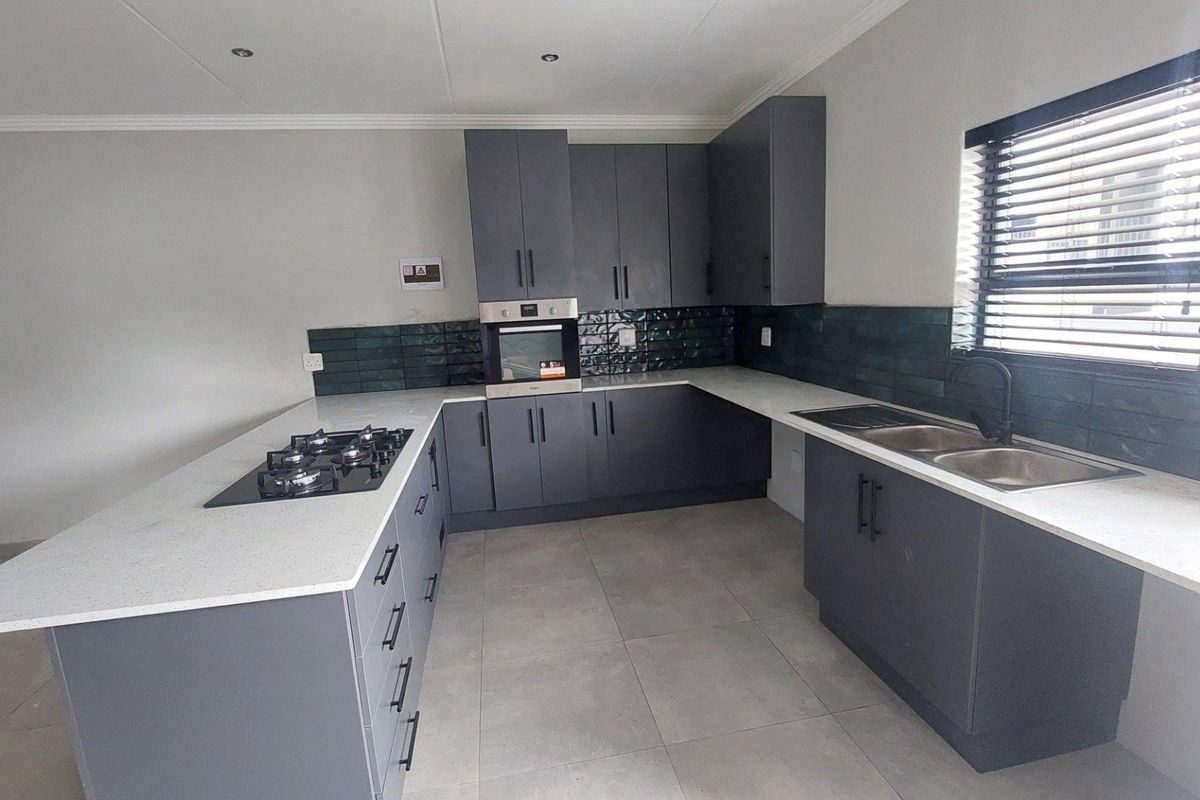 Modern kitchen featuring dark grey cabinetry, white quartz countertops, a gas hob, built-in oven, and a double sink with a tiled backsplash.