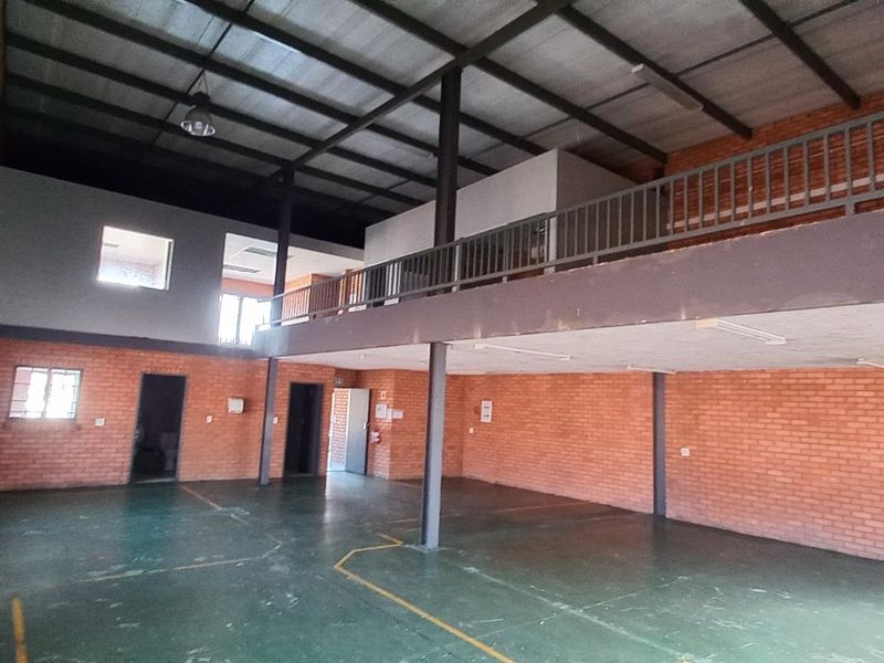 Spacious industrial warehouse unit featuring exposed brick walls, high ceilings, and a mezzanine level with metal railing, suitable for storage or workshop use.