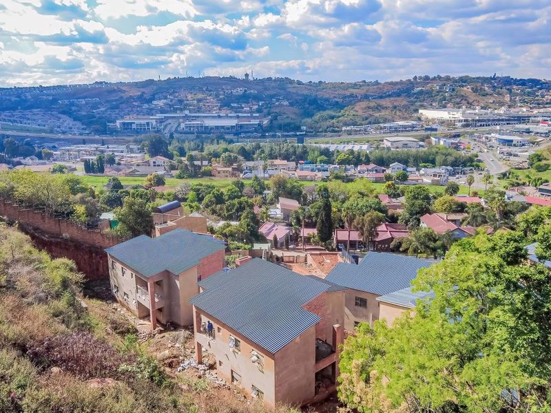 Aerial view of a residential development under construction, featuring multiple units with pitched metal roofs and brick exteriors overlooking a suburban landscape.