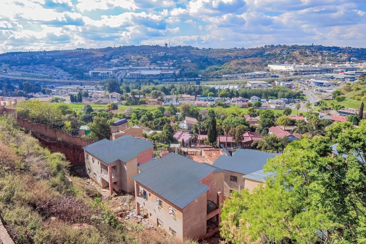 Aerial view of a residential development under construction, featuring multiple units with pitched metal roofs and brick exteriors overlooking a suburban landscape.
